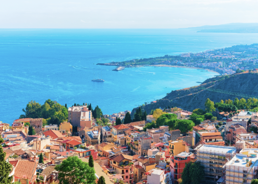 Bright houses with red roofs by the body of water and green hills. 